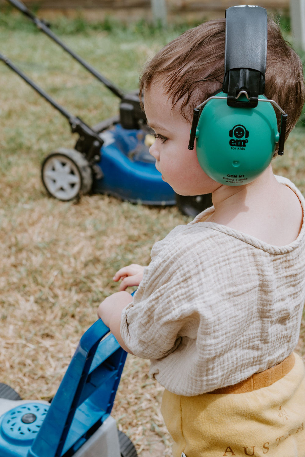 young boy wearing green protective earmuffs while pretending to mow lawns with father